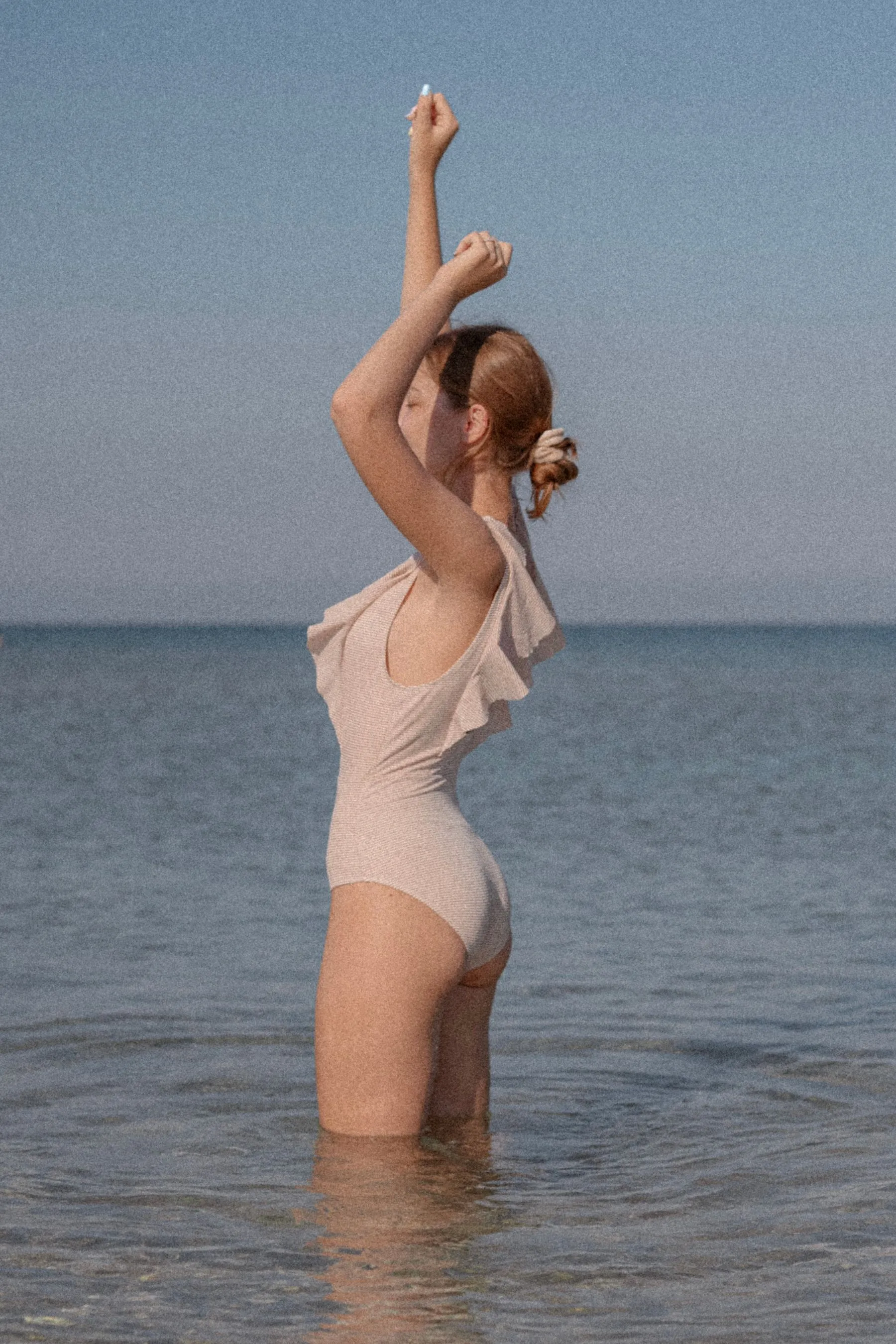 Femme en maillot une-pièce clair face à la mer